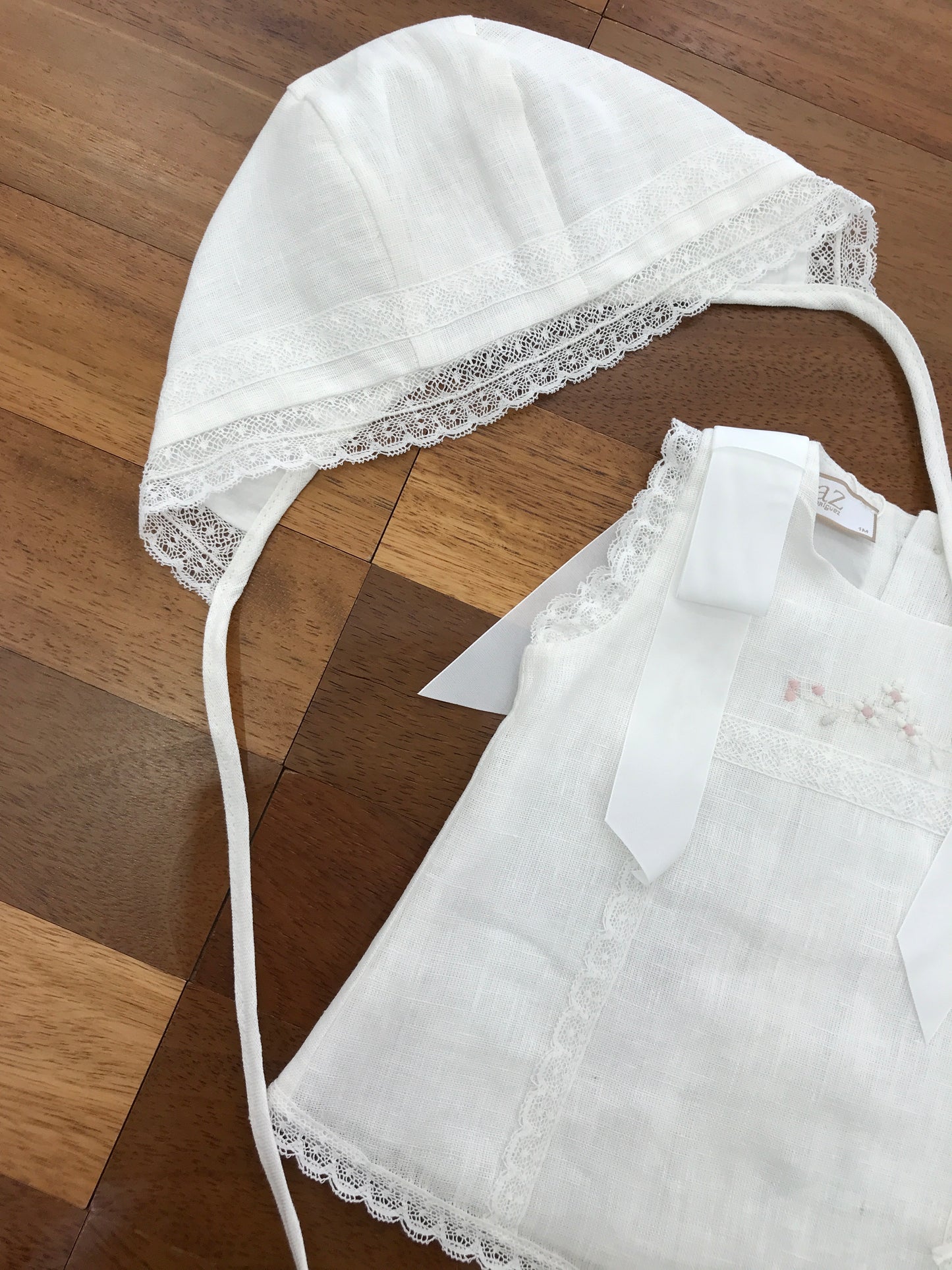 Completo Paz Rodriguez in lino bianco con fiocchi sulle spalle con merletto con fiori ricamati sul davanti con culotte e cuffia abbinata