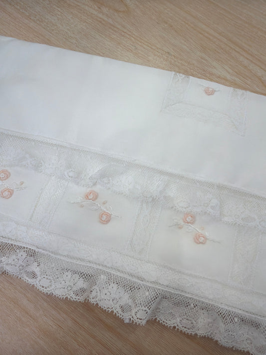 Lenzuolino Piccola Giuggiola in battista di cotone bianco con rifiniture in pizzo piccoli riquadri con roselline rosa ricamate