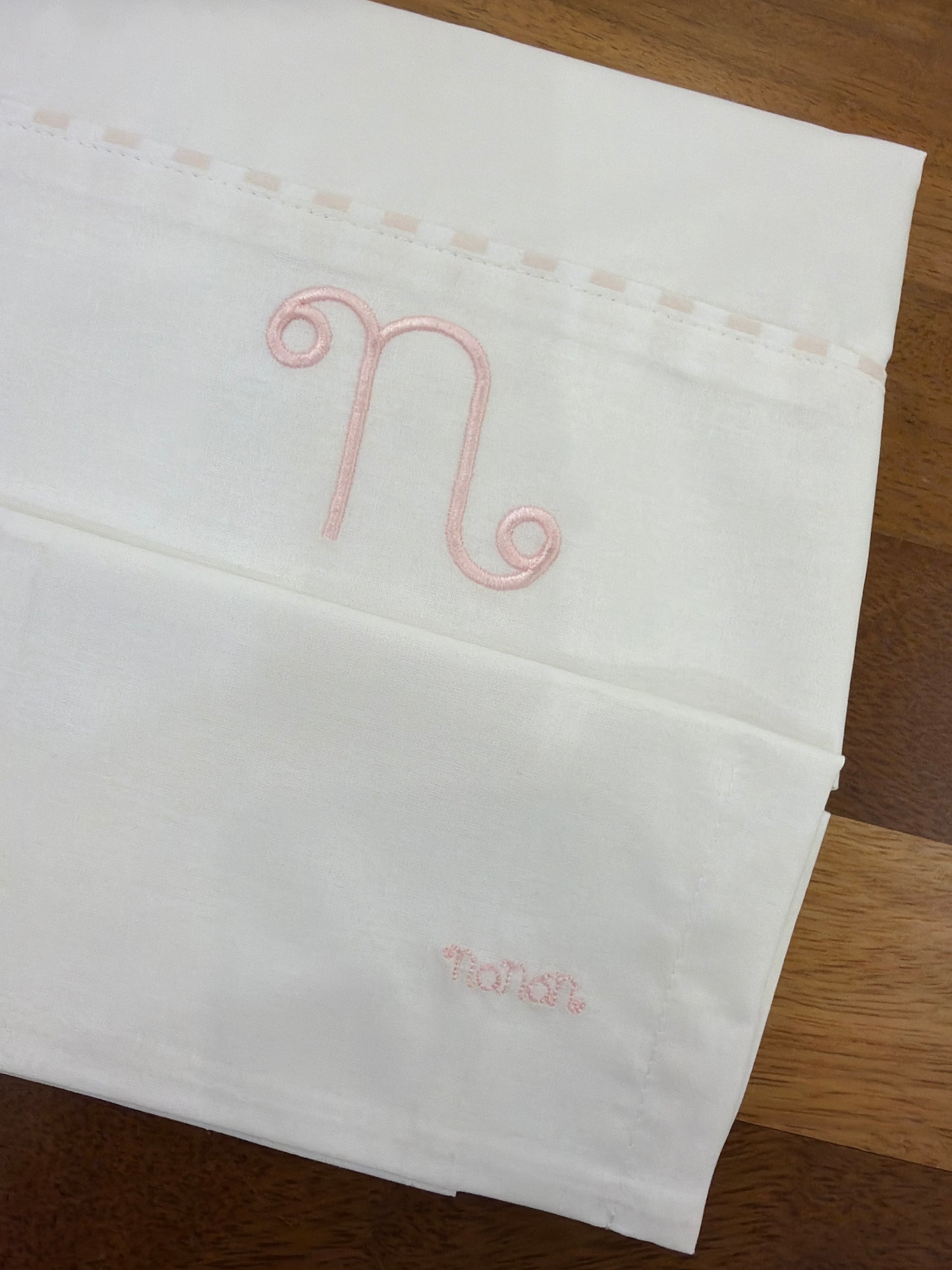Lenzuolino Nanan in cotone bianco e rosa con logo nanan ricamato su federa passanastro su lenzuolino rosa
