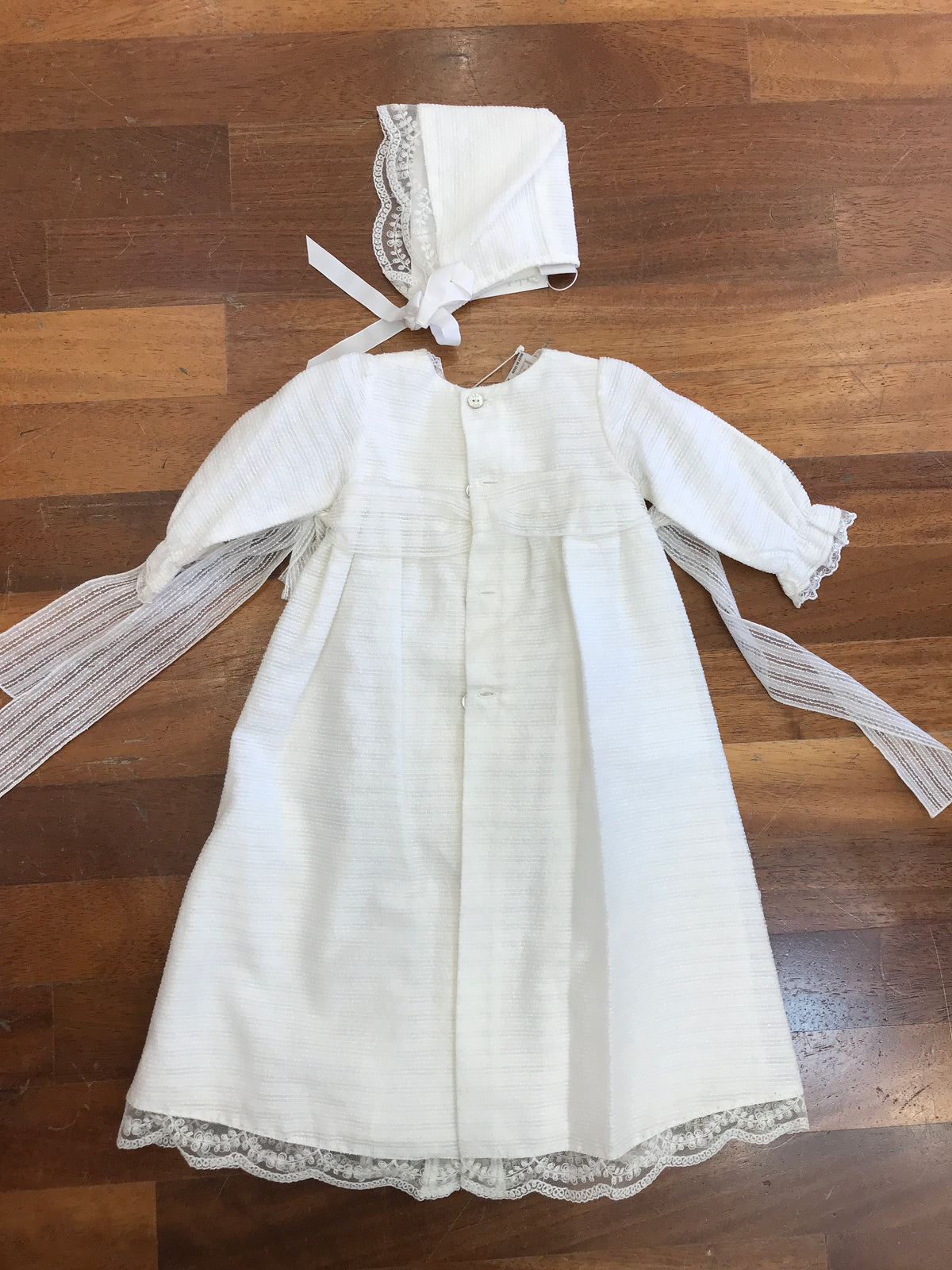 Abito lungo Paz Rodriguez in battista di cotone manica lunga con fiocchetti laterali pizzo e cuffietta coordinata