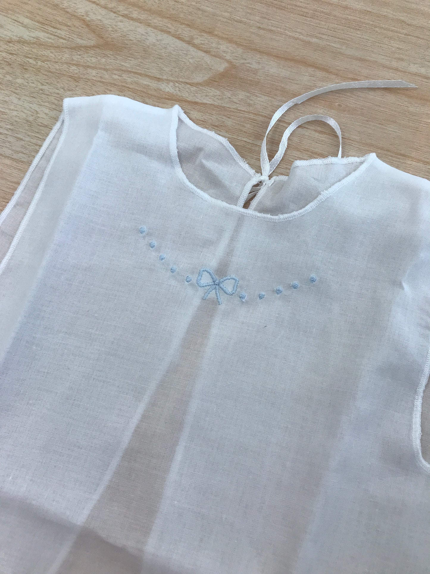 Camicino Baby gi in cotone bianco smanicato con pois e fiocchetto celeste ricamato al centro sul davanti