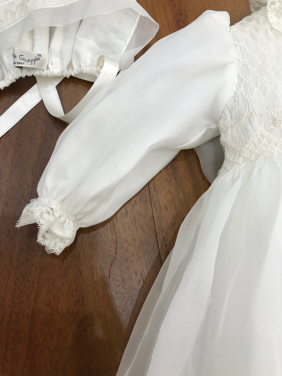 Abito lungo Piccola Giuggiola in organza in seta con gonna lavorata da pizzo corpetto manica lunga con lavorazione di punto smock e roselline ricamate a mano con cuffia coordinata e con punto smock