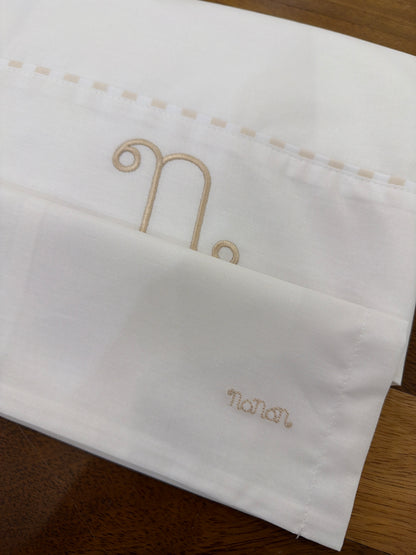 Lenzuolino Nanan in cotone bianco con logo nanan beige sulla federa con passanastro su lenzuolino