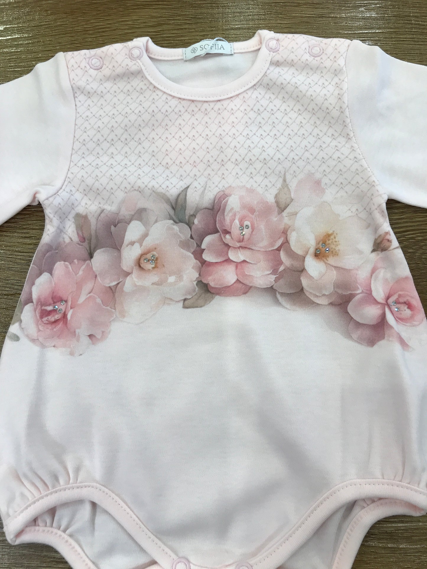 Pagliaccetto Sofija in caldo cotone rosa con camelie sul davanti