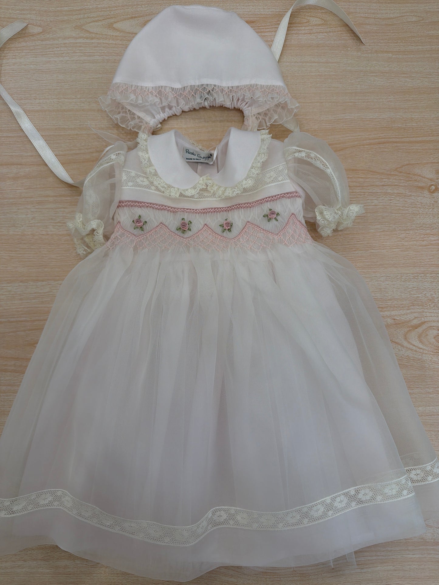 Abito Piccola Giuggiola in organza in seta rosa con applicazione di pizzo sul gonnellone e corpetto con lavorazione di punto smock e fiori ricamati con cuffietta abbinata