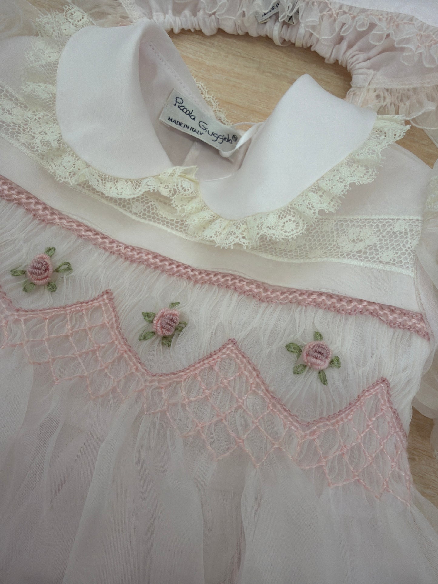 Abito Piccola Giuggiola in organza in seta rosa con applicazione di pizzo sul gonnellone e corpetto con lavorazione di punto smock e fiori ricamati con cuffietta abbinata