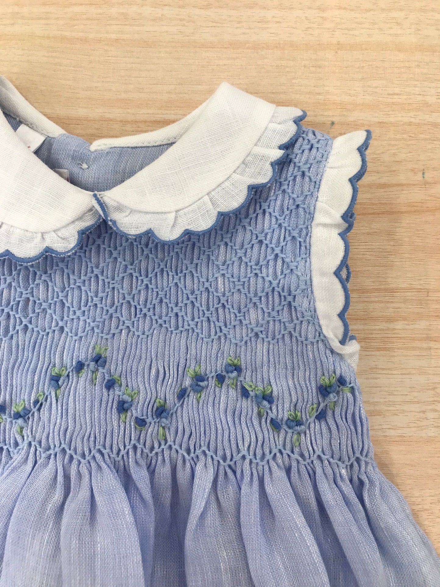 Abito Les Enfants de Gisele in lino smanicato con rusche bianche con colletto bianco e rusche rifinita in celeste  con corpetto lavorato da punto smock e fiorellini bianchi ricamati