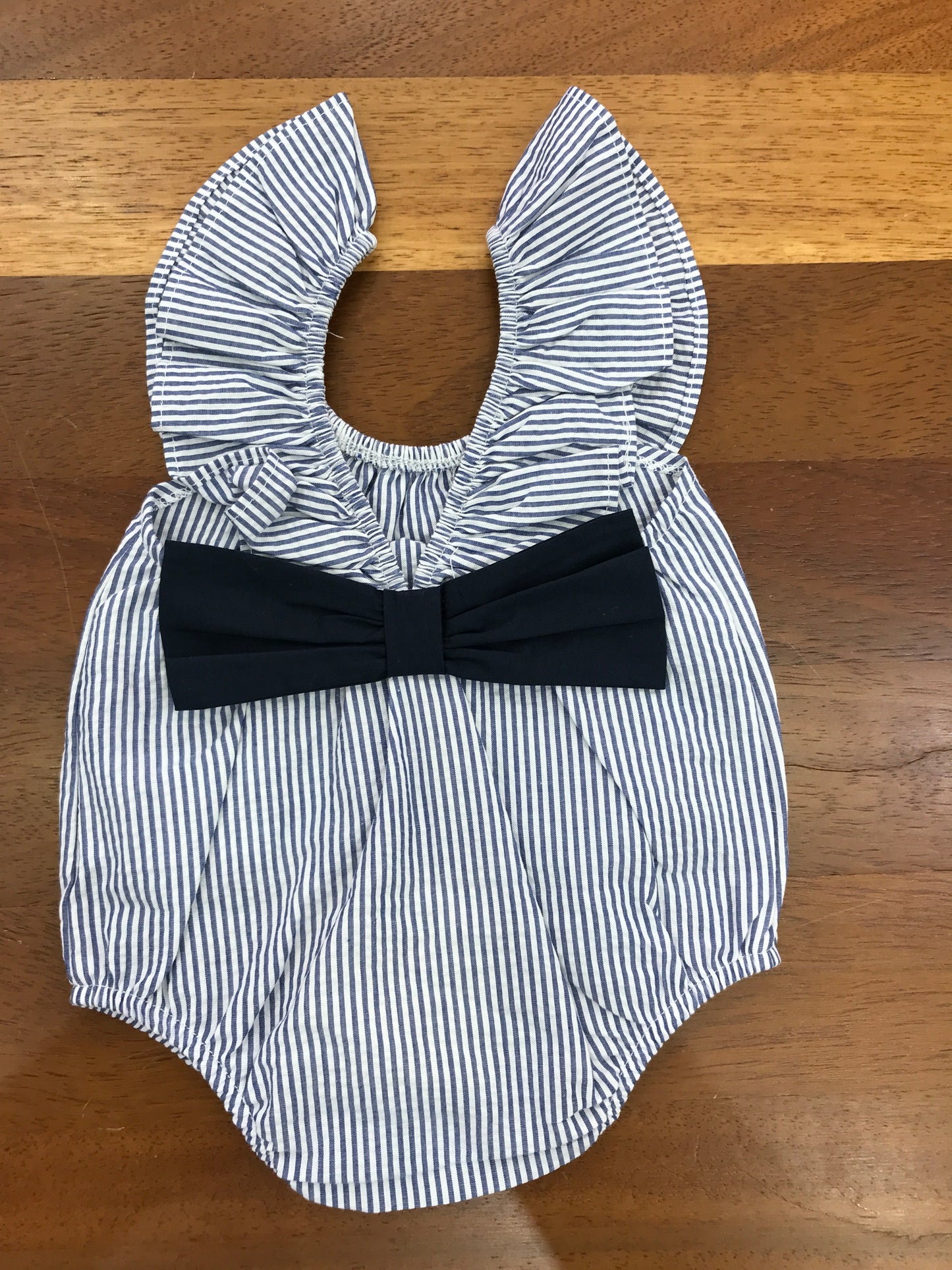 Pagliaccetto Nanan in cotone bianco e blu a righe smanicato con fiocco blu sul retro