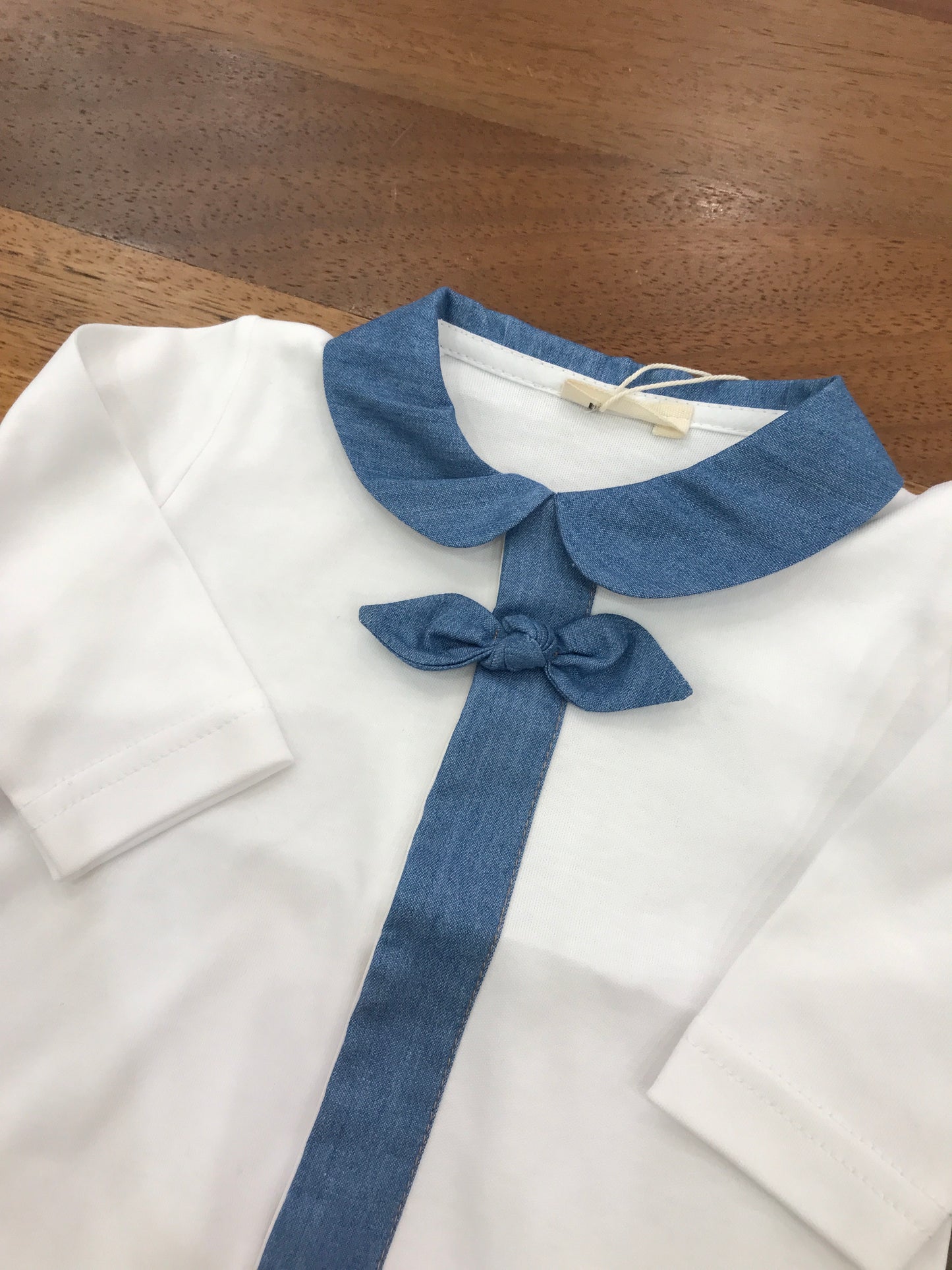 Tutina Baby Gi in cotone bianca gamba lunga con piedini manica lunga con collo tondo in  denim lo stesso profilo del colletto viene riportato sul davanti della tutina