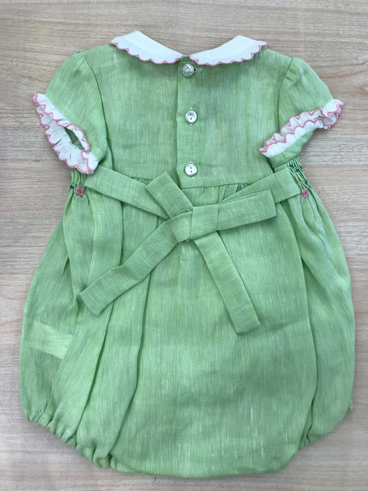 Pagliaccetto Les Enfants de Gisele in lino verde con rusche bianche rifinite in rosa con lavorazione di punto smock e rose
