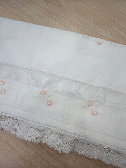 Lenzuolino Piccola Giuggiola in battista di cotone bianco con rifiniture in pizzo piccoli riquadri con roselline rosa ricamate