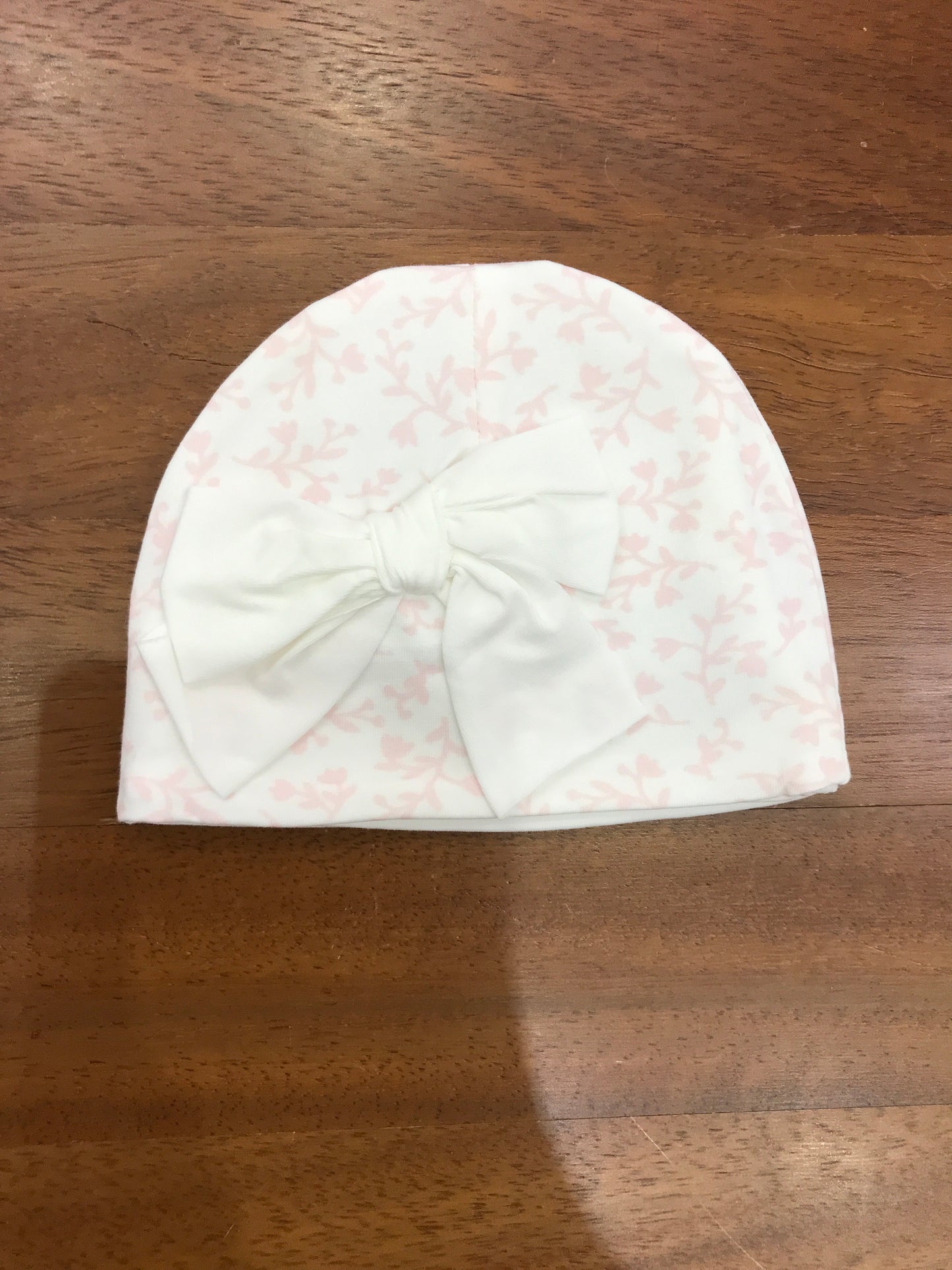 Cappello Le Bebè in cotone bianco con fiori rosa e fiocco centrale bianco sul davanti