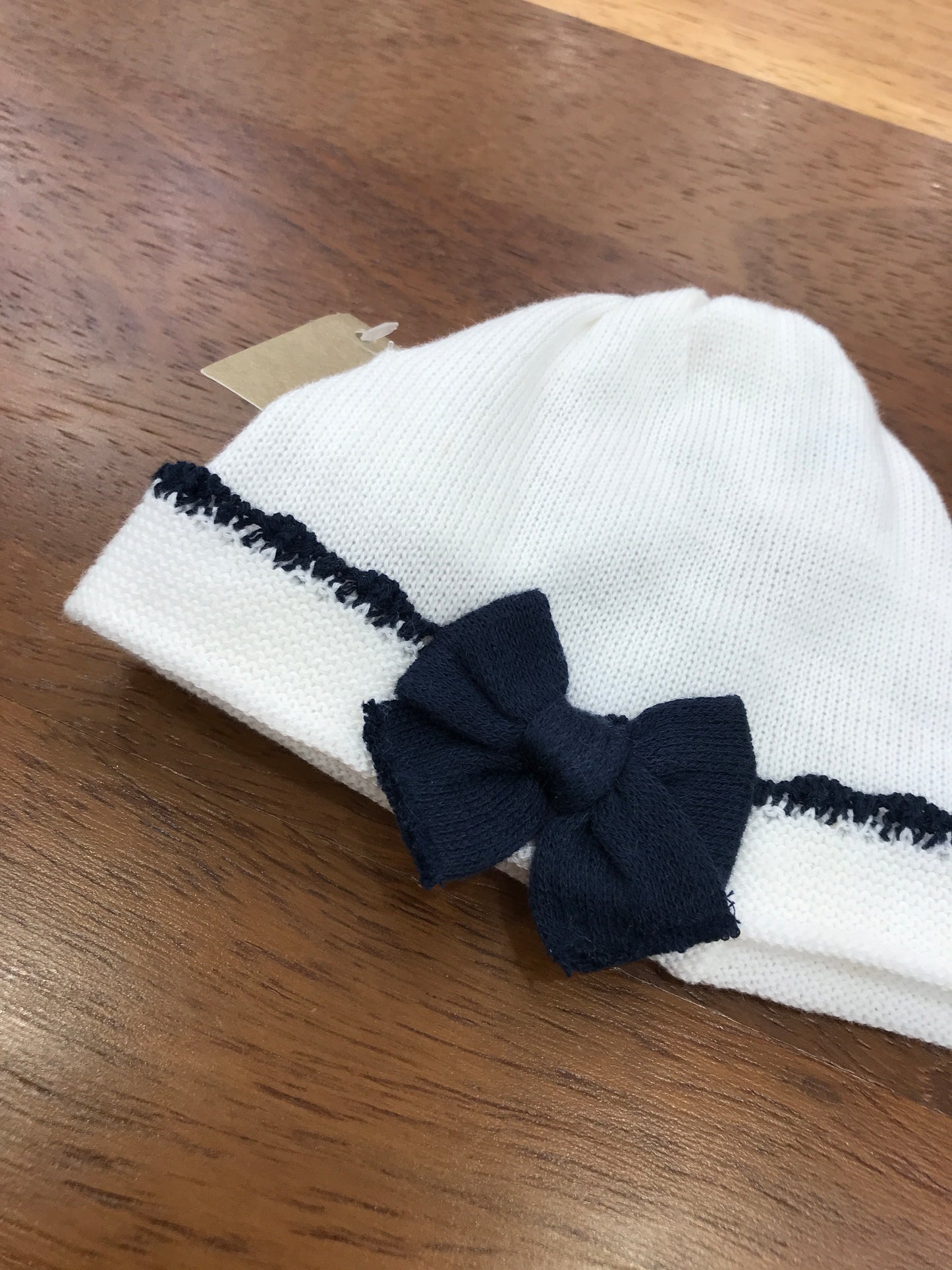 Cappello Baby Lord in filo bianco con risvolto con rifinitura blu scuro con fiocchetto applicato al centro blu scuro