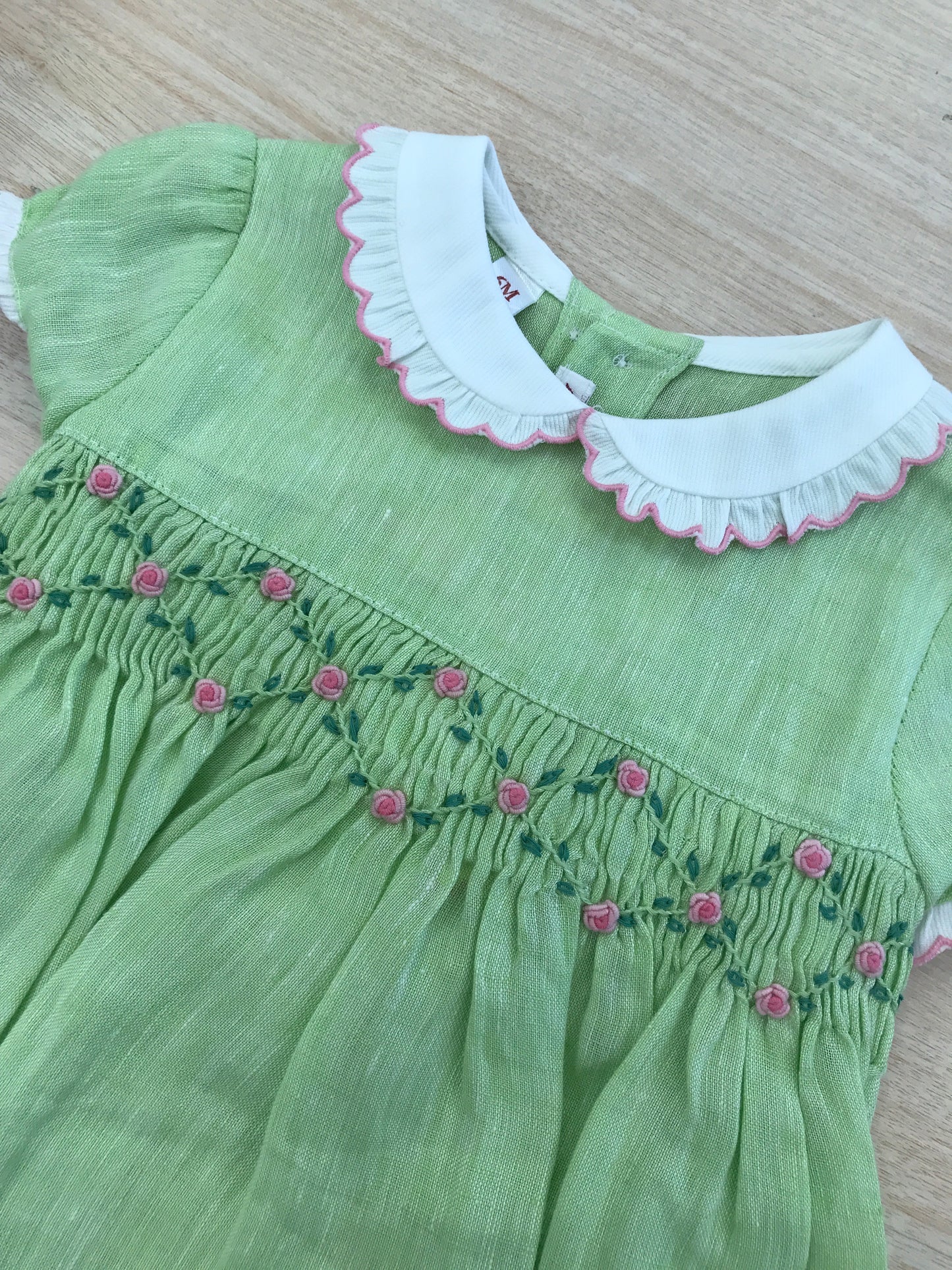 Pagliaccetto Les Enfants de Gisele in lino verde con rusche bianche rifinite in rosa con lavorazione di punto smock e rose