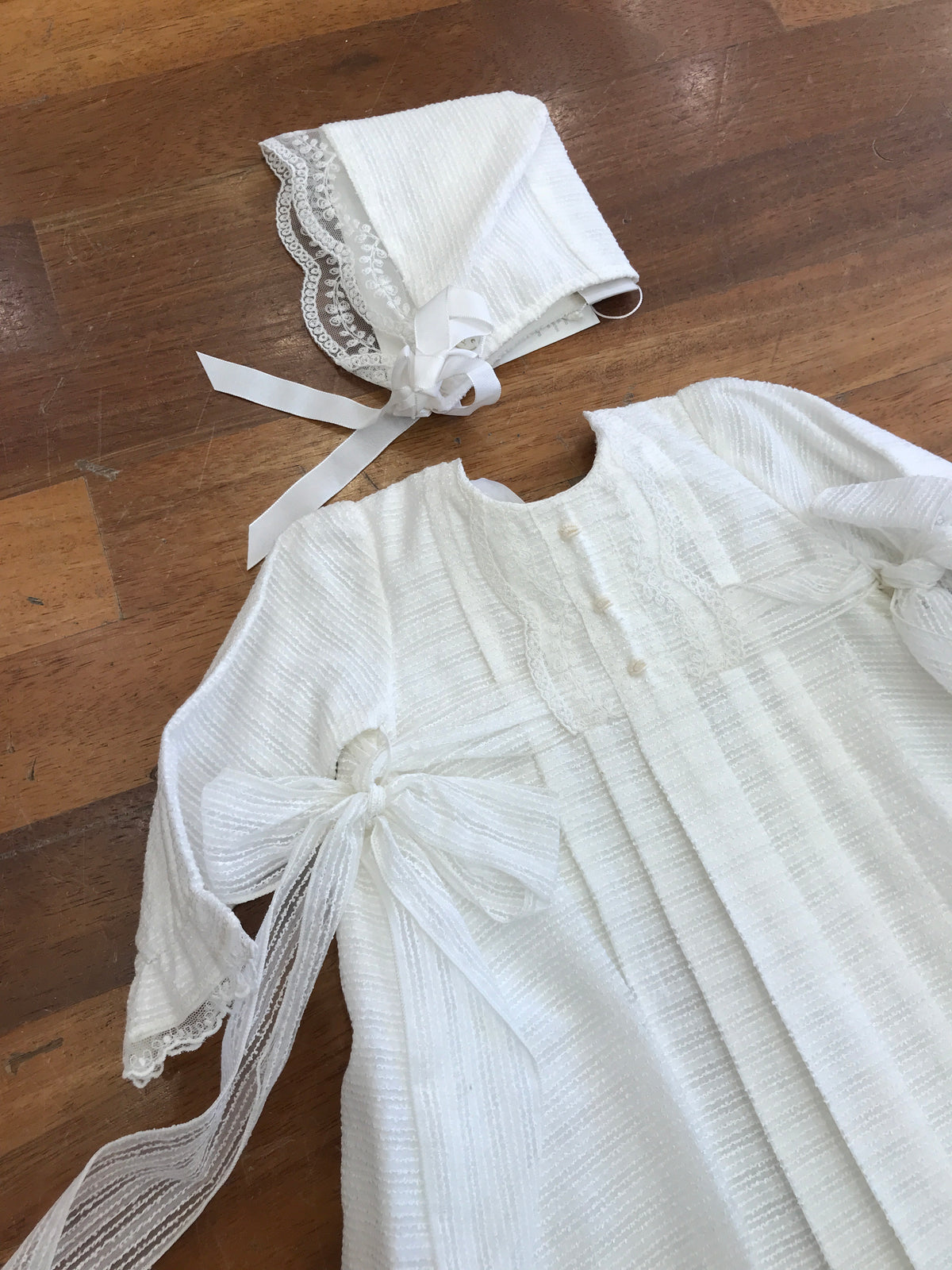 Abito lungo Paz Rodriguez in battista di cotone manica lunga con fiocchetti laterali pizzo e cuffietta coordinata