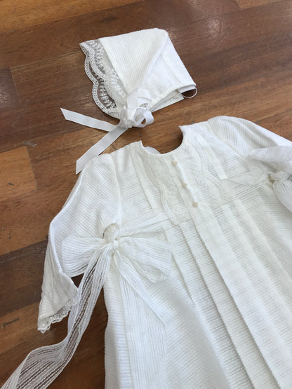 Abito lungo Paz Rodriguez in battista di cotone manica lunga con fiocchetti laterali pizzo e cuffietta coordinata